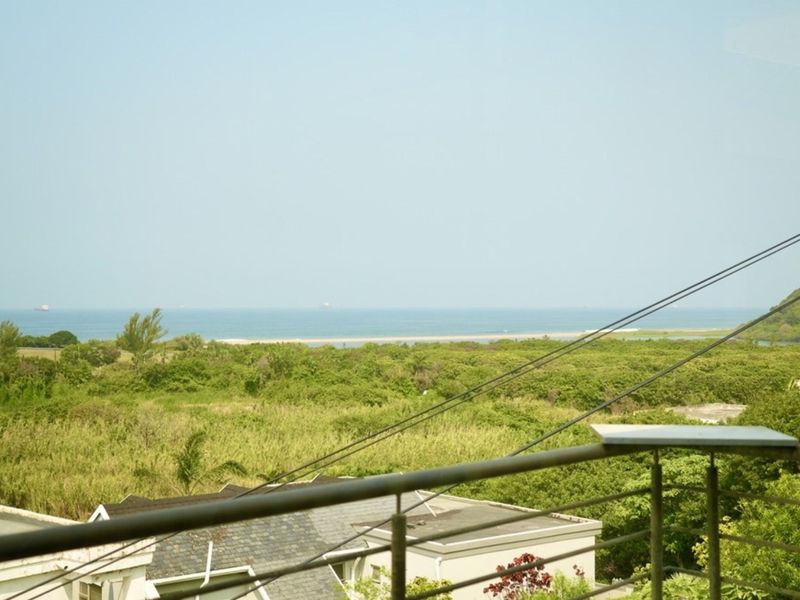 Elevated view overlooking lush coastal vegetation and the ocean, framed by a metal balcony railing.