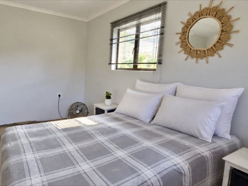 A bright bedroom featuring laminate flooring, neutral walls, and venetian blinds, offering a clean and functional space.