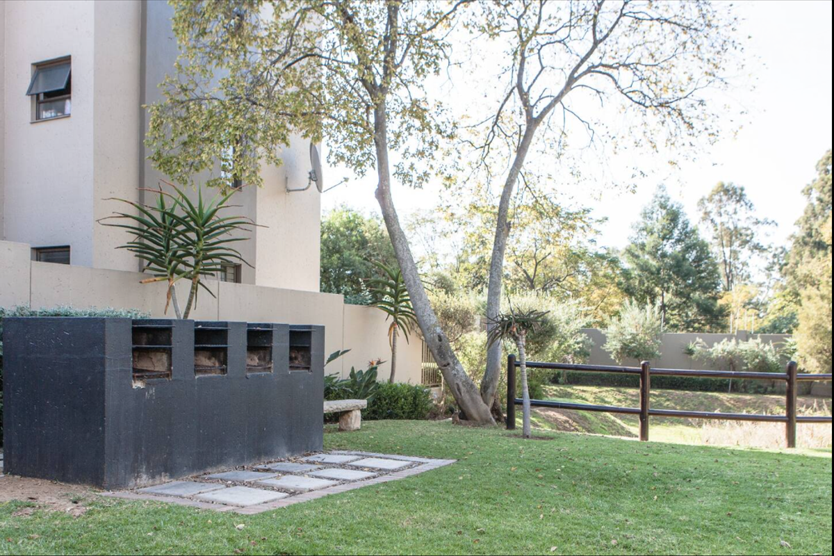 Rear garden area featuring a built-in braai, paved base, and perimeter boundary wall with timber fencing.