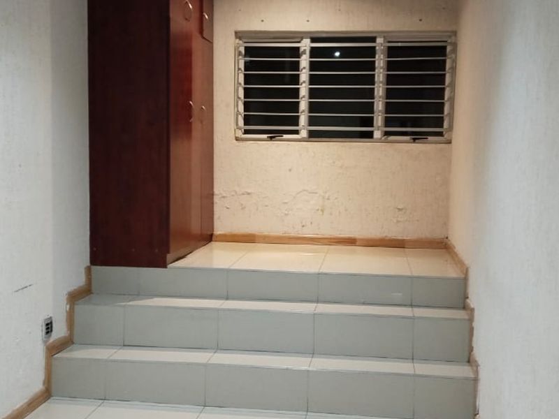 An empty bedroom featuring tiled steps leading to a raised area, a built-in cupboard, and a window with security bars.