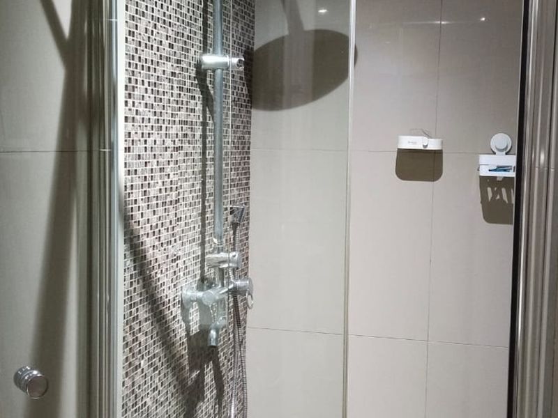 A modern shower enclosure featuring a rain shower head, chrome mixer, and a decorative mosaic tiled feature wall.