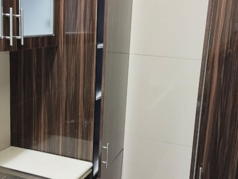 A compact kitchen area featuring modern wood-grain cabinetry, a stainless steel sink, and clean tiled wall finishes.