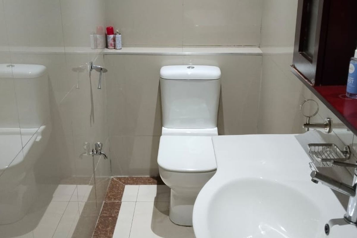 A functional bathroom featuring a white toilet, vanity basin with a modern mixer tap, and neutral wall and floor tiling.