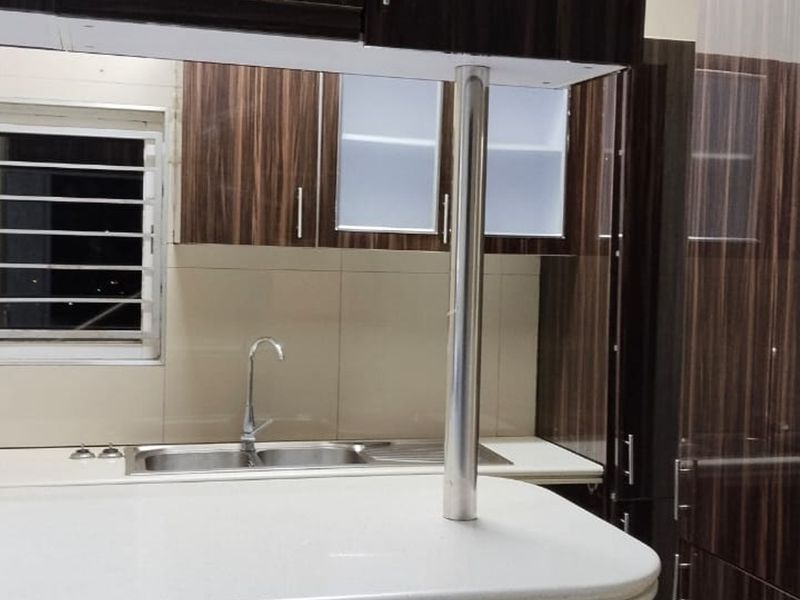 A modern kitchen featuring dark wood-grain cabinetry, a stone countertop, stainless steel sink, and a breakfast bar with a metal support pillar.