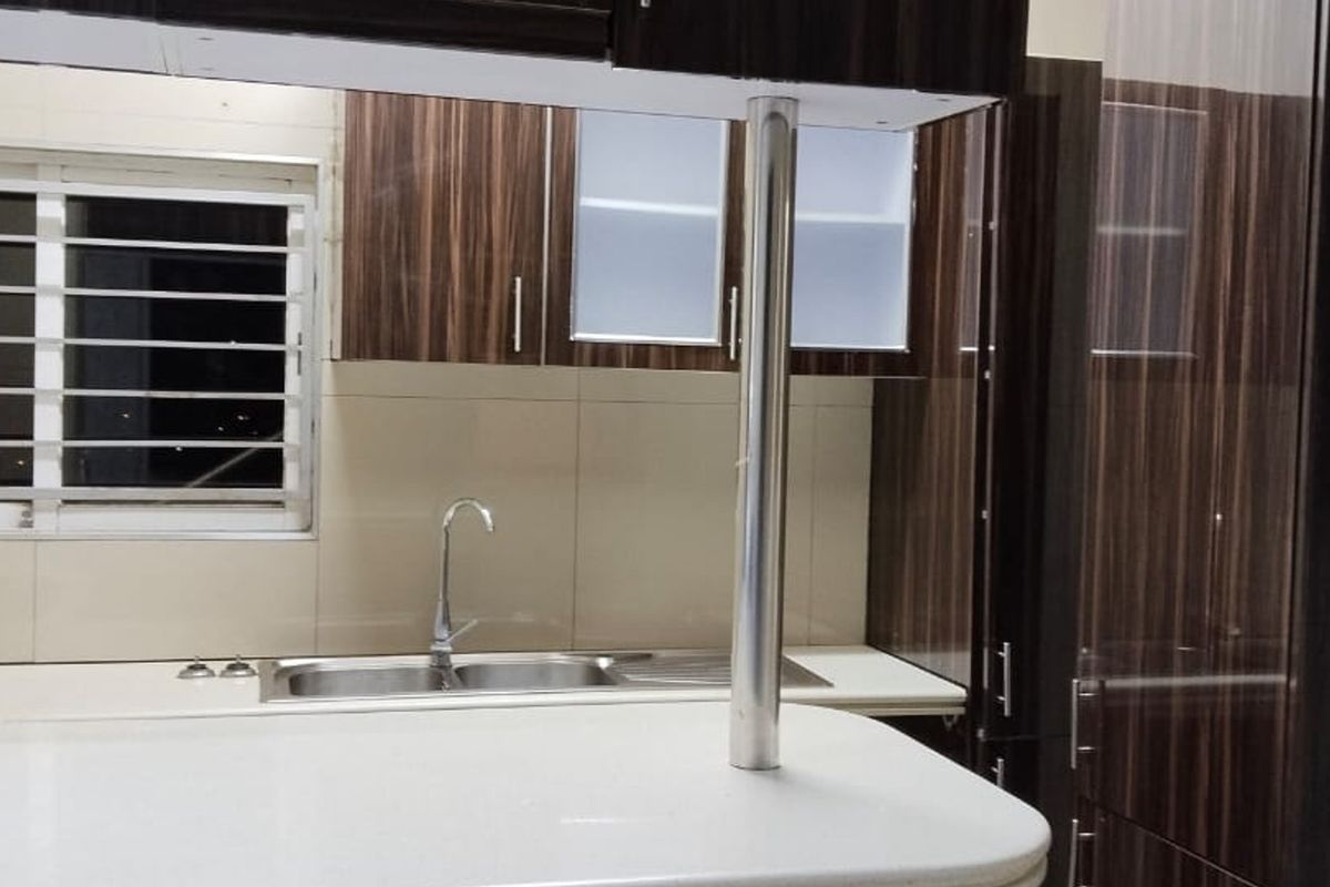 A modern kitchen featuring dark wood-grain cabinetry, a stone countertop, stainless steel sink, and a breakfast bar with a metal support pillar.