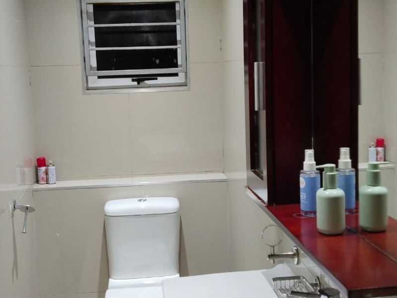 A functional bathroom featuring tiled walls, a vanity mirror, and a louvered window for ventilation.