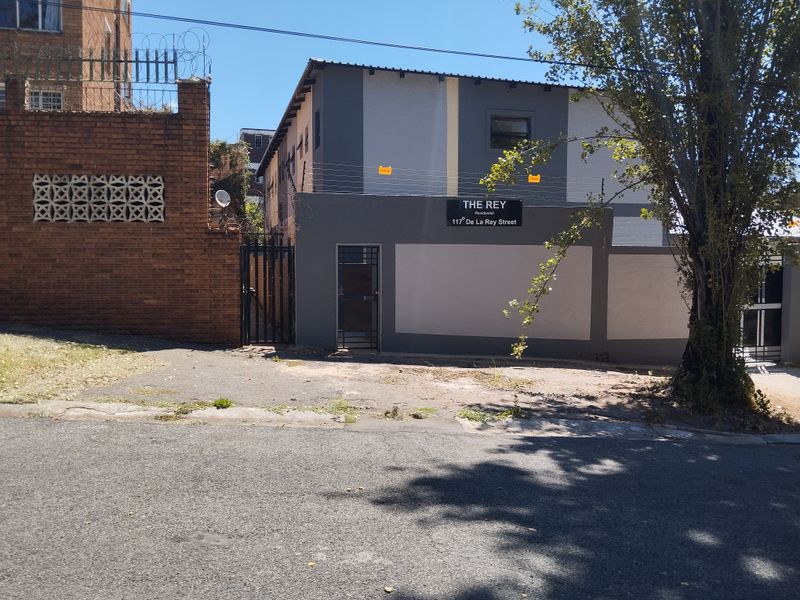 Street view of the apartment complex entrance featuring a perimeter wall, electric fencing, and paved access area.