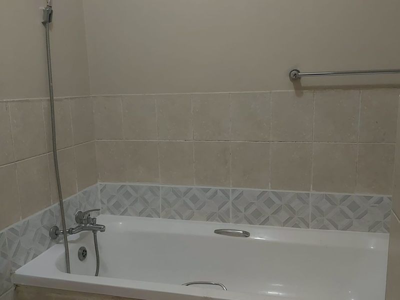 A functional bathroom featuring a built-in bathtub with a shower mixer and decorative wall tiling.