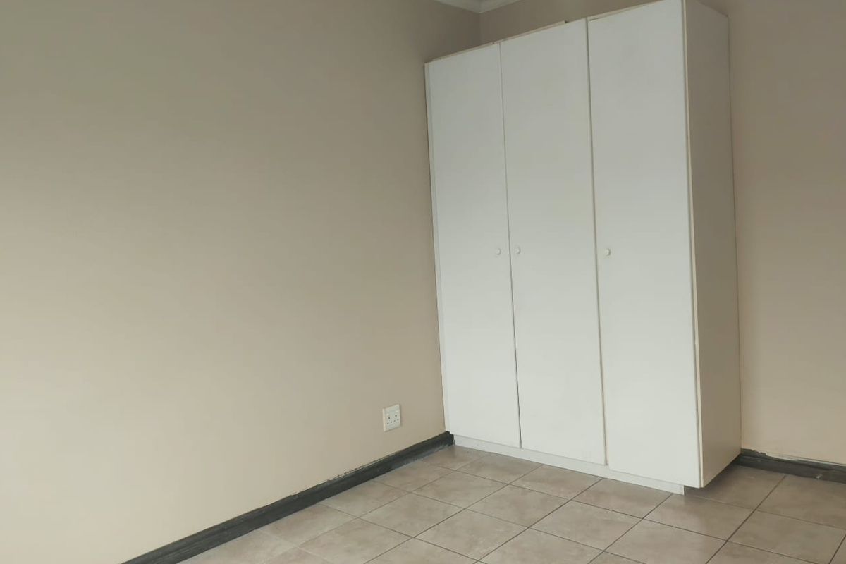 A clean, empty bedroom featuring neutral walls, tiled flooring, and a white built-in wardrobe with ample storage space.