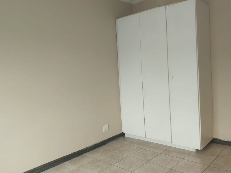 A clean, empty bedroom featuring neutral walls, tiled flooring, and a white built-in wardrobe with ample storage space.