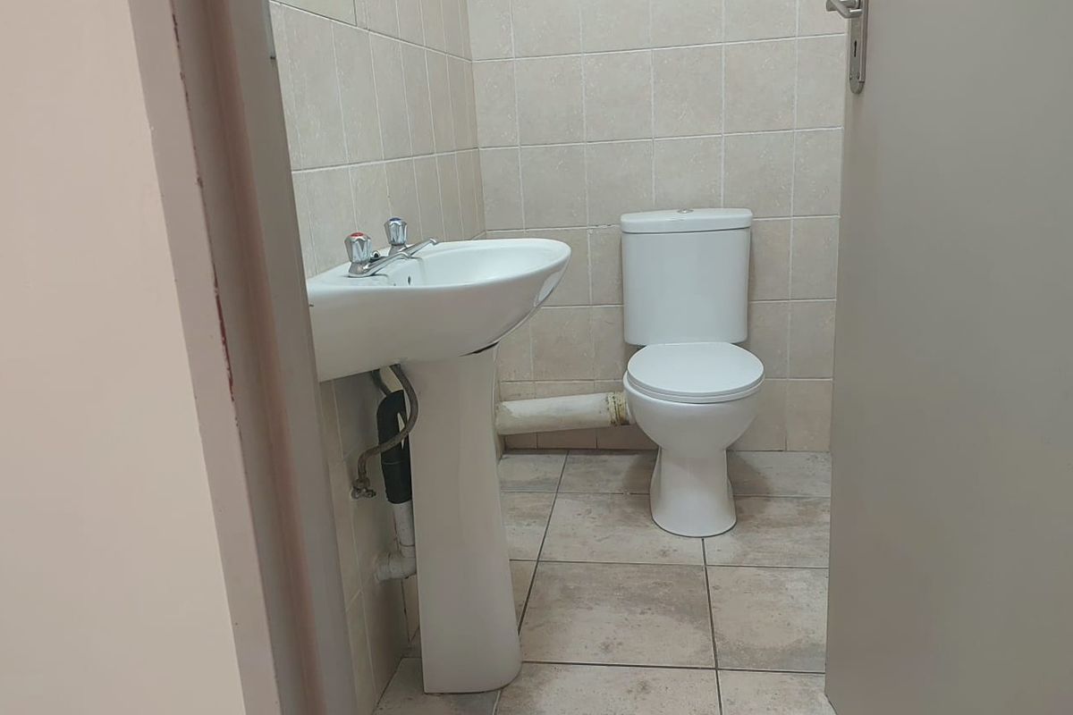 A compact bathroom featuring a pedestal basin and a dual flush toilet with neutral ceramic wall and floor tiling.