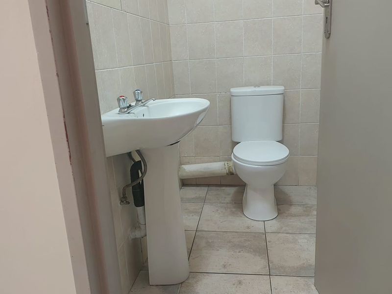 A compact bathroom featuring a pedestal basin and a dual flush toilet with neutral ceramic wall and floor tiling.