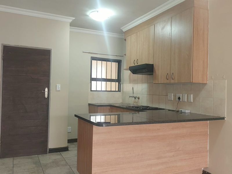 A functional kitchen featuring light wood cabinetry, dark granite countertops, a built-in hob, and an extractor fan, finished with neutral wall tones and tiled flooring.