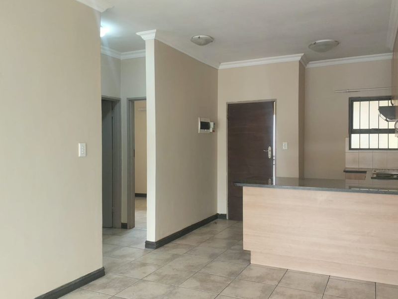 An open-plan living and kitchen area featuring tiled flooring, neutral walls, and a functional kitchen layout with a breakfast bar.