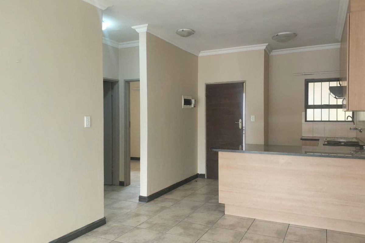 An open-plan living and kitchen area featuring tiled flooring, neutral walls, and a functional kitchen layout with a breakfast bar.