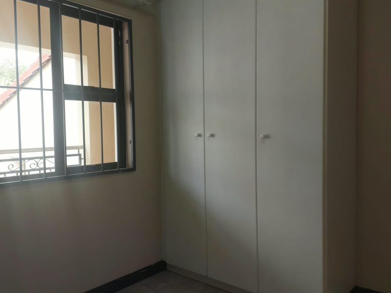 A clean, empty bedroom featuring built-in cupboards, tiled flooring, and a window fitted with security bars.