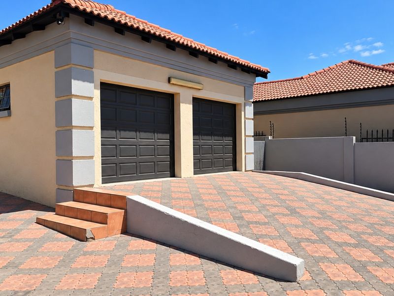 A well-maintained double garage featuring dark panelled doors, a tiled roof, and a paved driveway with integrated concrete steps and retaining wall.