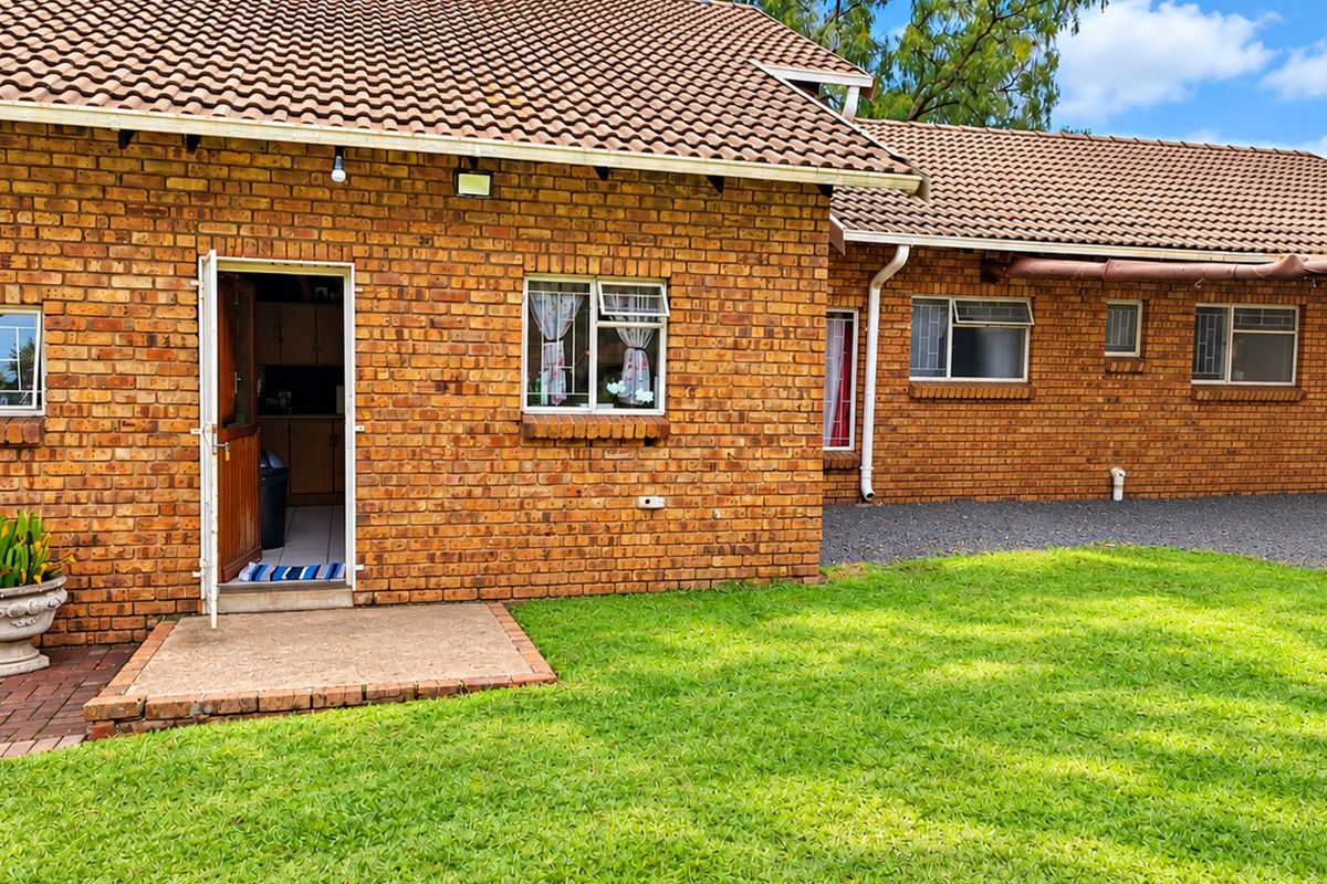 Rear view of a face brick house featuring a tiled roof, concrete patio area, and well-maintained lawn with paved pathways.