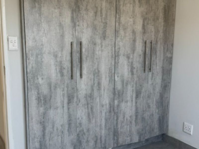 A bedroom featuring modern grey textured built-in wardrobes with sleek metal handles and integrated electrical fixtures.