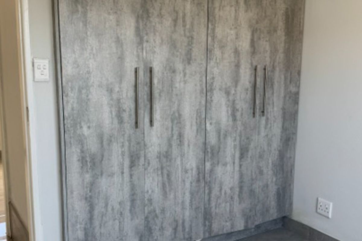 A bedroom featuring modern grey textured built-in wardrobes with sleek metal handles and integrated electrical fixtures.