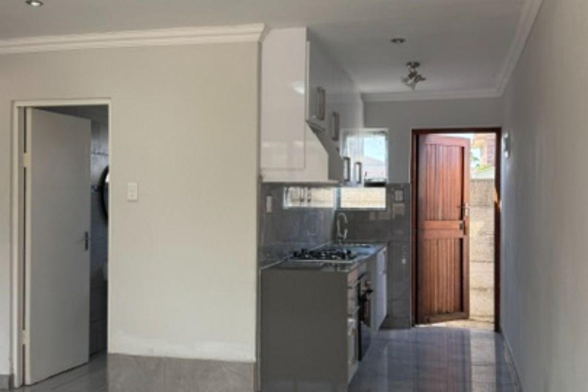 A compact, modern kitchen featuring sleek cabinetry, a gas hob, extractor fan, and tiled splashbacks, leading directly to an exterior door.
