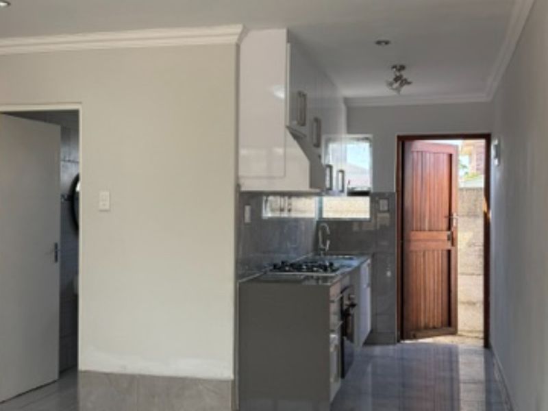 A compact, modern kitchen featuring sleek cabinetry, a gas hob, extractor fan, and tiled splashbacks, leading directly to an exterior door.
