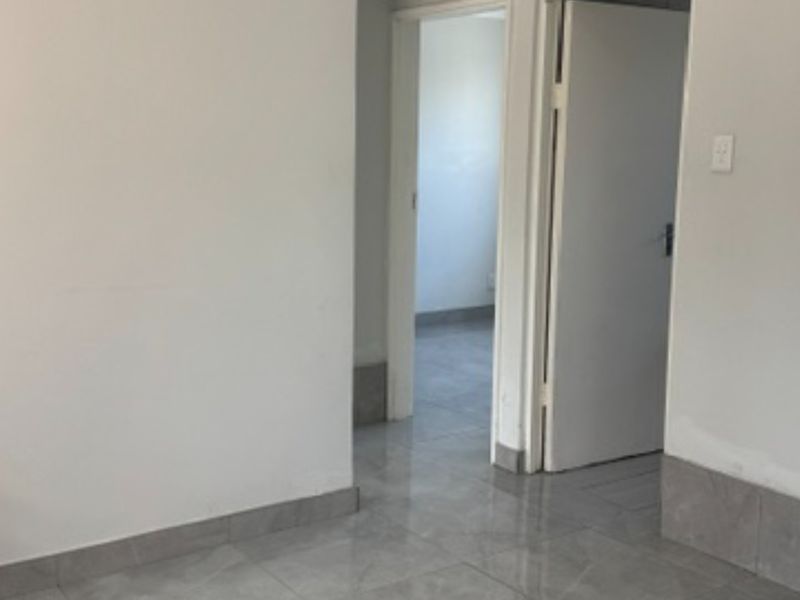 A clean, empty hallway featuring neutral tiled flooring and white interior doors, providing a simple transition between rooms.