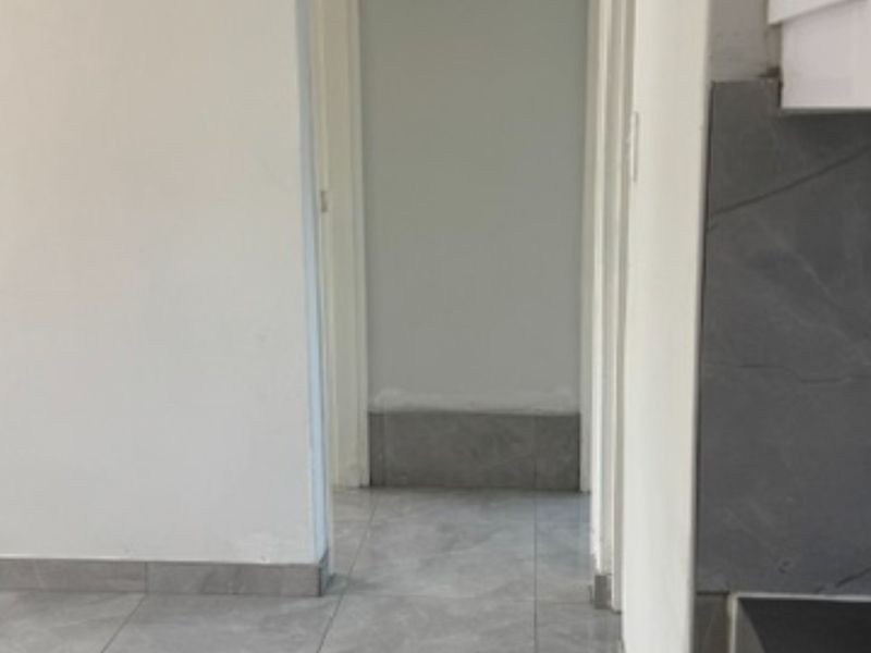 A view of a hallway featuring grey tiled flooring and matching skirting, with unfinished wall paint visible near the base.