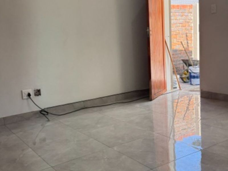An empty living area featuring modern grey tiled flooring, neutral walls, and a doorway leading to an outdoor space.