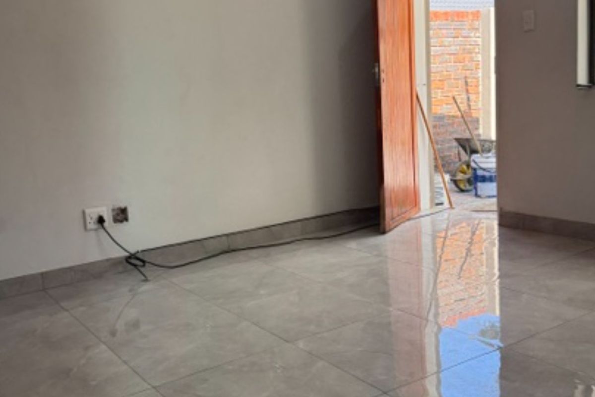An empty living area featuring modern grey tiled flooring, neutral walls, and a doorway leading to an outdoor space.
