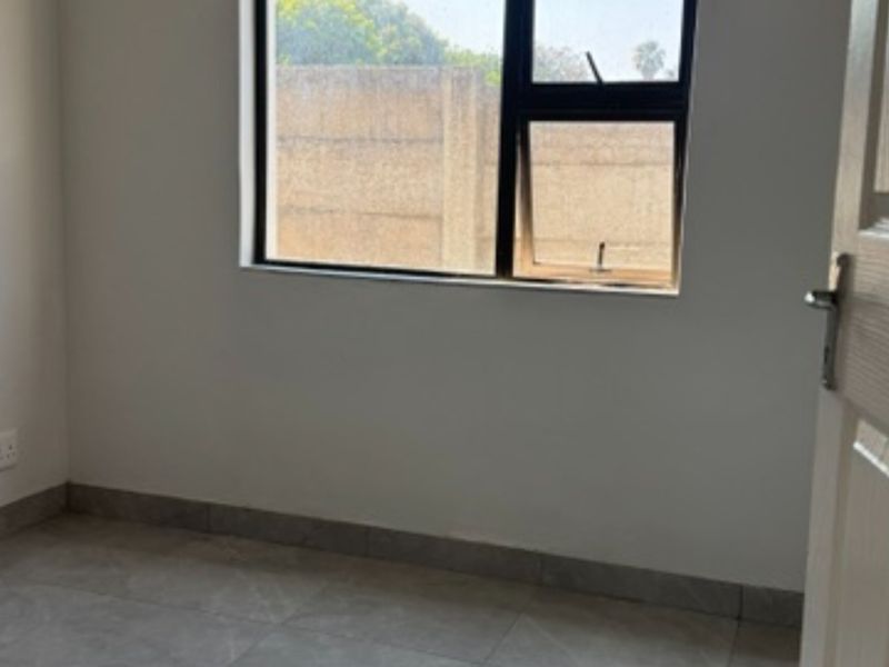 A clean, empty bedroom featuring neutral tiled flooring, white walls, and an aluminium-framed window providing natural light.