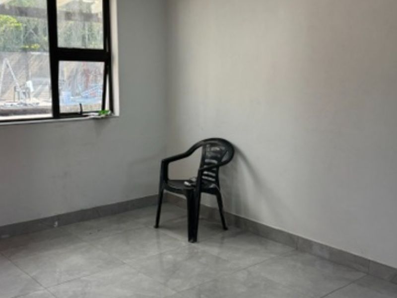 A bright, empty living area featuring neutral tiled flooring and a large aluminium-framed window, offering a blank canvas for interior design.