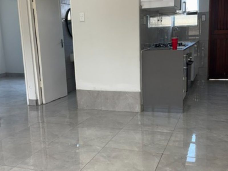 Open plan living area featuring modern grey porcelain floor tiles and a compact kitchen with built-in cabinetry, gas hob, and oven.