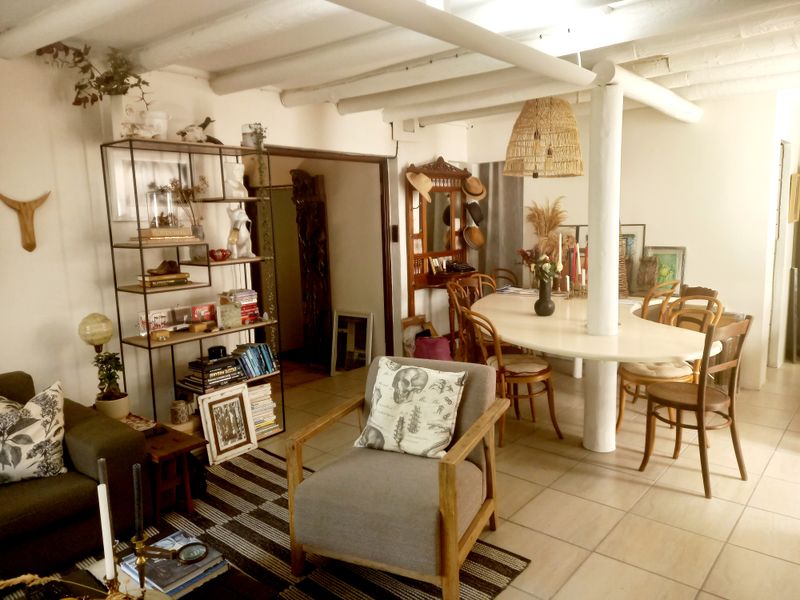 Open-plan living and dining area featuring exposed ceiling beams, a central support column, and neutral ceramic floor tiles.