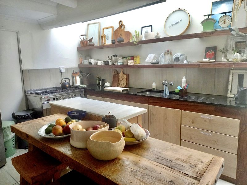 A functional kitchen featuring light wood cabinetry, black granite countertops, a gas stove, and open wooden shelving under a bright skylight.