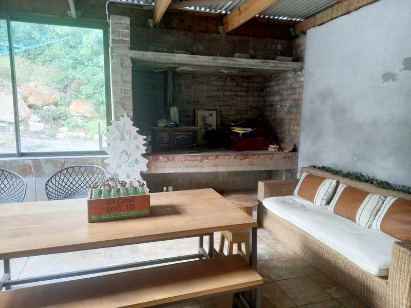 Covered outdoor patio area featuring a large built-in brick fireplace, tiled flooring, and exposed timber roof structure with access to the garden.