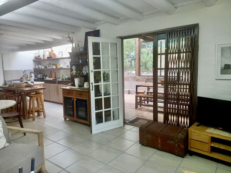 Open-plan living and kitchen area featuring exposed beam ceilings, tiled flooring, and direct access to an outdoor patio through French doors.