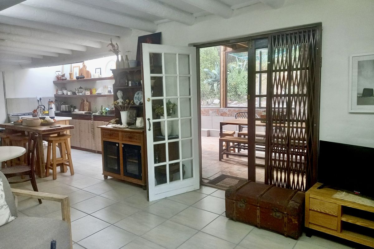 Open-plan living and kitchen area featuring exposed beam ceilings, tiled flooring, and direct access to an outdoor patio through French doors.