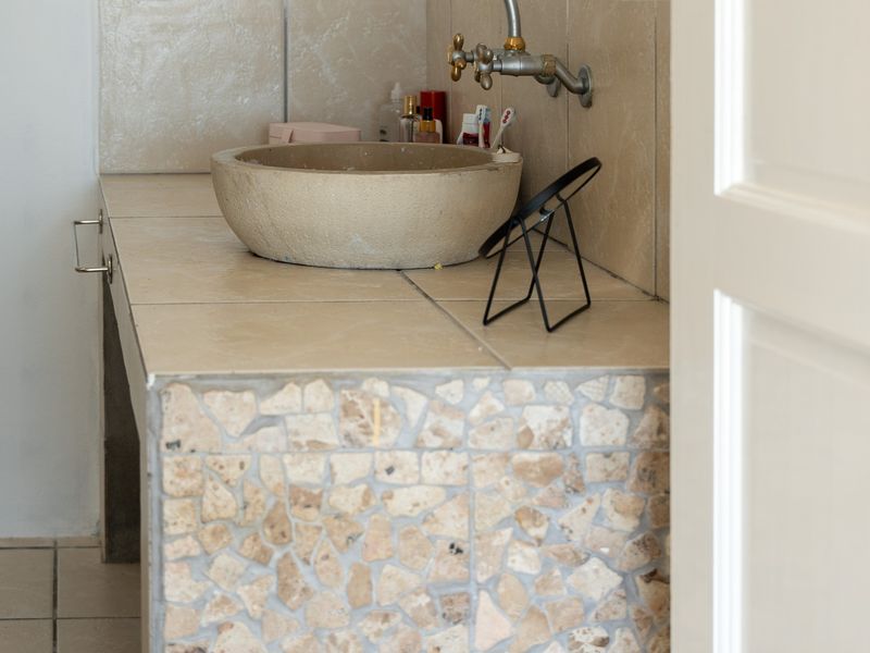 Bathroom vanity area featuring a stone vessel sink, wall-mounted faucet, and a tiled countertop with a stone mosaic base.