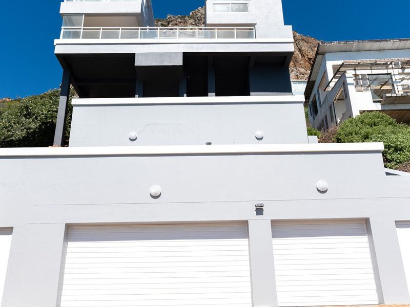 Front elevation of a multi-level apartment building featuring a double garage, modern grey facade, and upper-level balcony with glass balustrades.