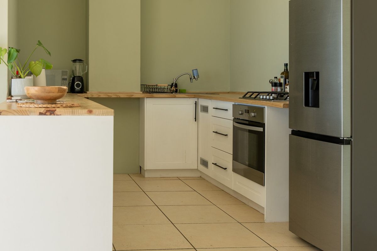 A functional kitchen featuring white cabinetry, wooden countertops, a built-in oven with gas hob, and tiled flooring.
