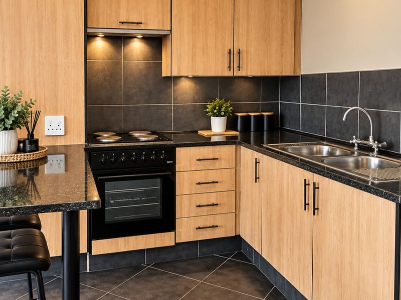 Modern kitchen featuring light wood cabinetry, dark granite countertops, integrated oven and hob, and a double sink with tiled backsplash.