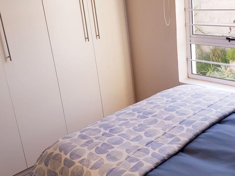A bedroom featuring white built-in cupboards and a window with security bars, providing natural light and storage space.