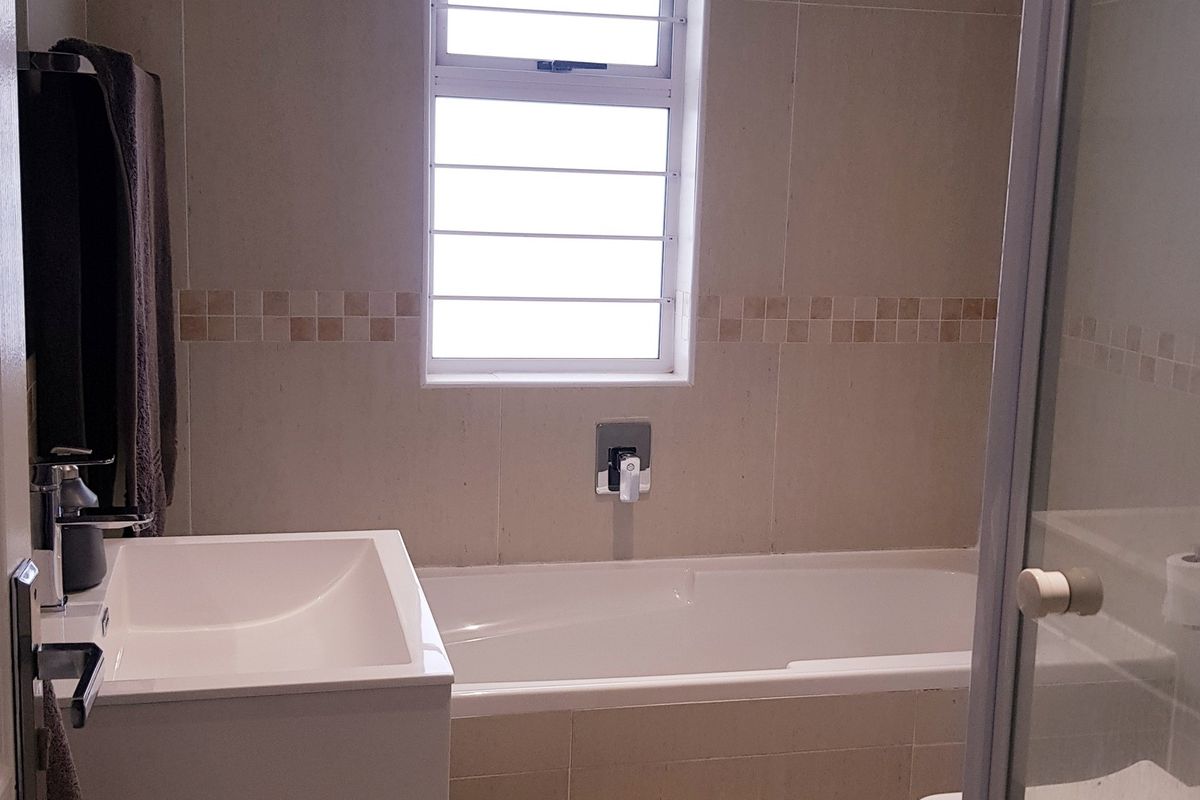 A clean, modern bathroom featuring a built-in bathtub, wall-mounted basin, and a separate shower enclosure with neutral wall tiling.