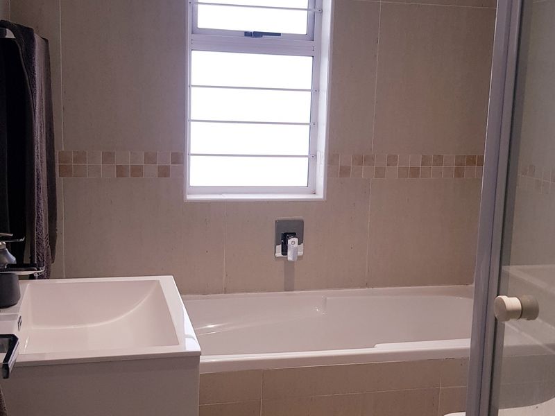 A clean, modern bathroom featuring a built-in bathtub, wall-mounted basin, and a separate shower enclosure with neutral wall tiling.
