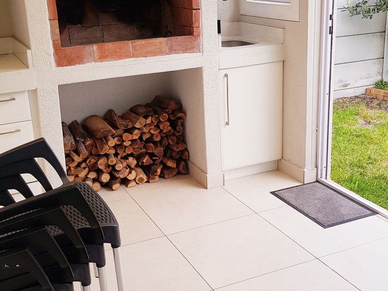 Covered patio area featuring a built-in brick braai, integrated sink, cabinetry, and tiled flooring, with direct access to the garden.