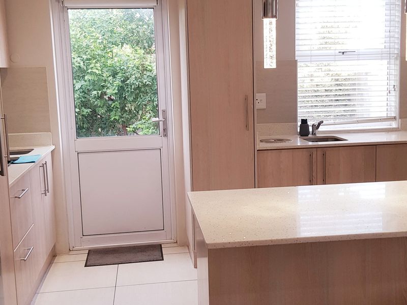 Modern kitchen featuring light wood cabinetry, stone countertops, integrated appliances, and direct access to the garden through a glass-paneled door.