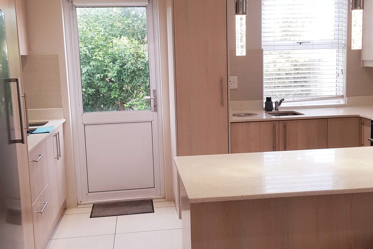 Modern kitchen featuring light wood cabinetry, stone countertops, integrated appliances, and direct access to the garden through a glass-paneled door.