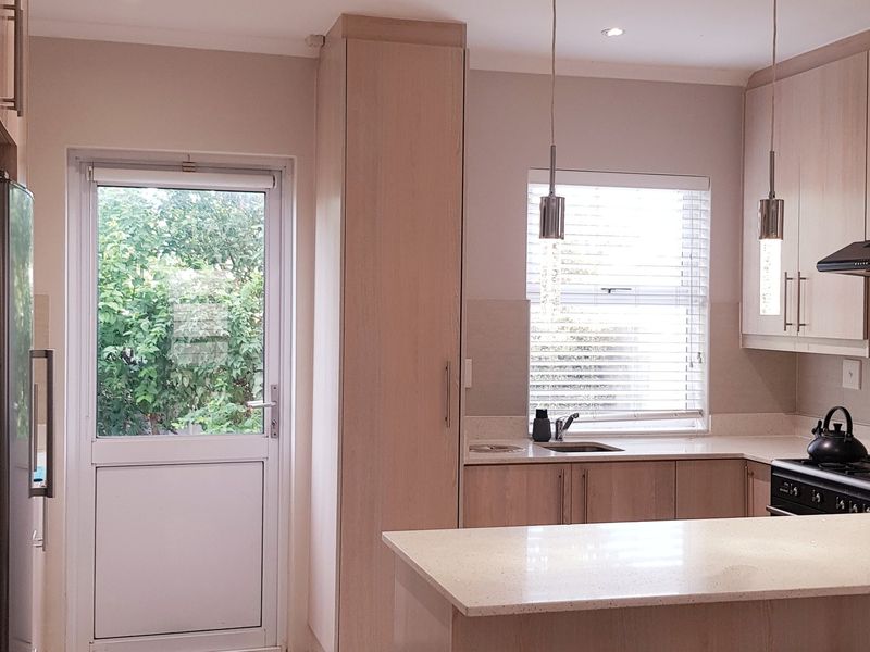 Modern kitchen featuring light wood cabinetry, stone countertops, integrated gas hob with extractor fan, and direct access to the garden.