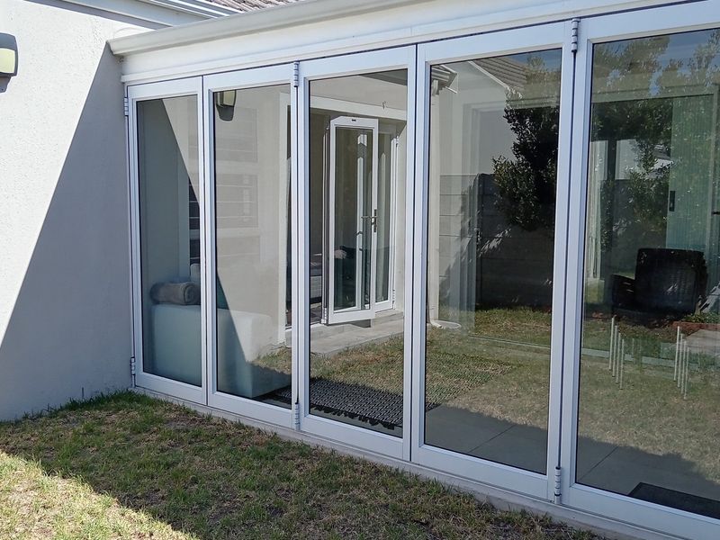 Rear view of the property featuring modern aluminium stacker doors opening onto a paved patio and garden area.